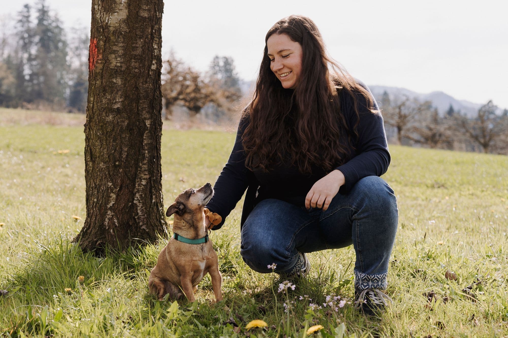 Liliane kniet bei ihrem Hund in der Natur